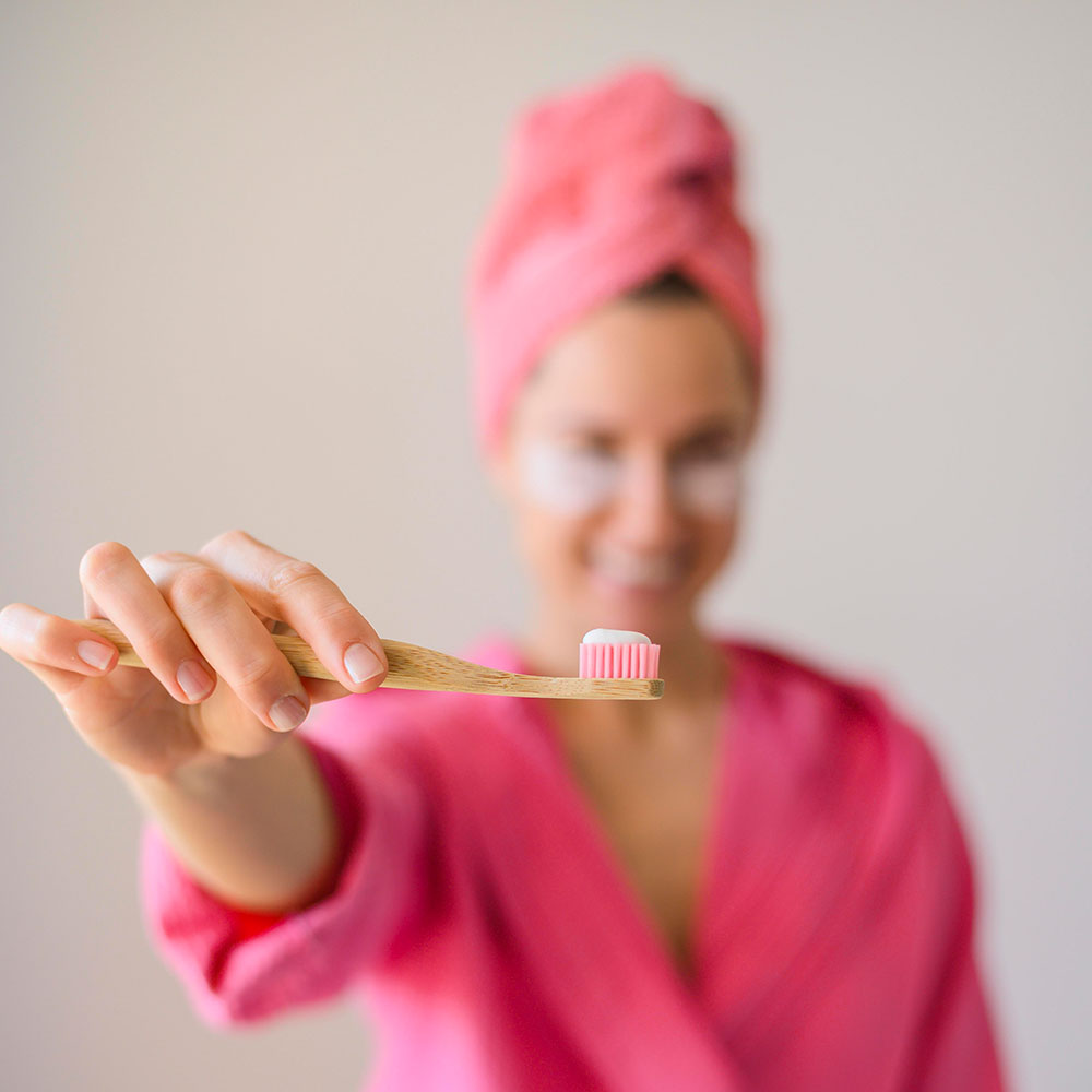Eine Frau im pinkfarbenen Bademantel zeigt ihre Zahnbürste